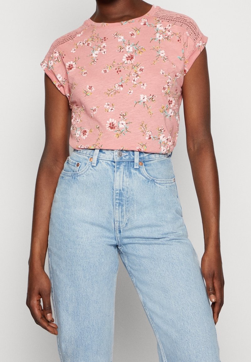 Lyserød blomstret kortærmet top med struktureret strikdetalje på skuldrene, parret med højtaljede lyseblå denim jeans.