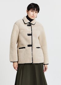 Veste en polaire beige texturée avec des accents noirs, dotée d'un col arrondi, de trois boutons et de deux poches avant.