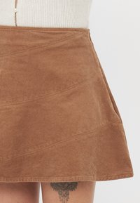 Bruine corduroy rok met een uitlopende vorm, voorzien van horizontale ribbels en stikseldetails. Valt boven de knie.