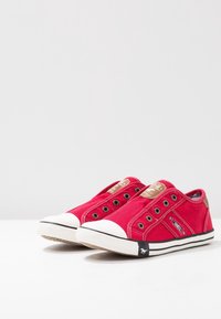 Paire de baskets rouges en toile à enfiler avec bouts en caoutchouc blanc, semelles rayées noires, œillets métalliques et écussons de marque sur la languette et le côté.