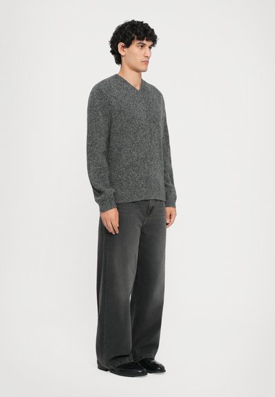 Gray knitted pullover with a V-neck, paired with loose-fitting dark denim jeans. The outfit has a textured fabric and relaxed silhouette.
