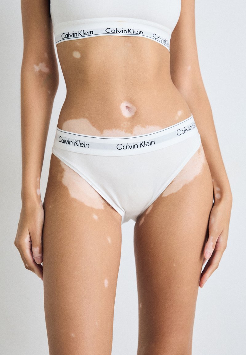 Vita bomullsunderkläder med en kontrasterande midjeresår med Calvin Klein-logotyp. Designen har en slät textur och en enkel, klassisk snitt.