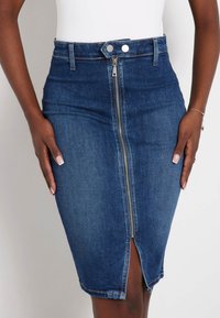 Tamsiai mėlynas džinsinis pieštuko sijonas su priekiniais užtrauktukais, aukštu liemeniu ir skeltu apatine dalimi. Pasižymi klasikiniu penkių kišenių dizainu.