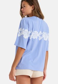 Lichtblauw katoenen t-shirt met korte mouwen, voorzien van een wit bloemenpatroon op de rug. Zachte textuur en een ontspannen pasvorm.