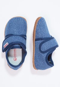 Niebieskie buty materiałowe o fakturze przypominającej dżins, z rzepem i brązową gumową podeszwą. Posiadają okrągły czubek i wyściółkę amortyzującą.