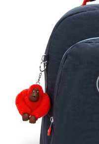 Marinblå ryggsäck med en röd, fluffig apnyckelring. Väskan har rundade kanter och en dragkedjeficka med en kontrasterande orange dragkedjepull.