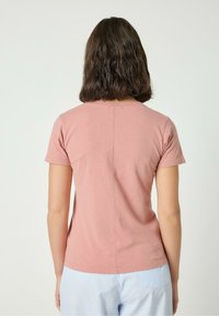 Różowy t-shirt z krótkim rękawem, okrągłym dekoltem i widocznymi przeszyciami, zestawiony z jasnoniebieskimi spodniami w paski.