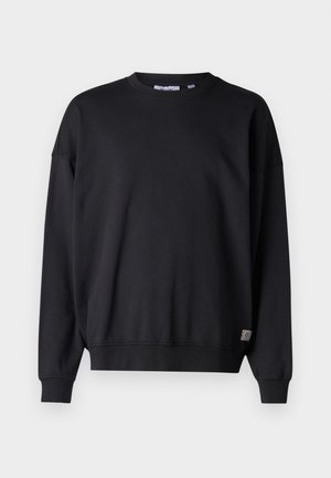 Sweatshirt noir à manches longues, col rond, avec des poignets et un ourlet côtelés. Fabriqué en tissu doux, il arbore un petit logo brodé en bas.