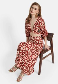 Conjunto de dos piezas en tonos rojos y beige con un crop top de escote en V profundo y una falda larga. La modelo lleva sandalias de tacón cuadrado metálicas doradas.