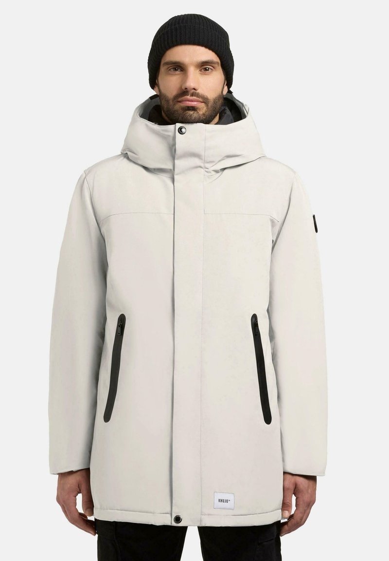 Lysegrå parka-jakke med hætte, der har sorte lynlåslommer, minimalistisk design og et sort mærke ved kanten. Struktureret stof.