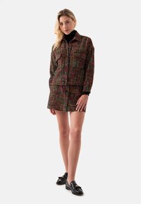 Multicolore tweed jasje en rok set met een geruit patroon, knoopsluiting en contrasterende zwarte mouwen. Gecombineerd met zwarte loafers.