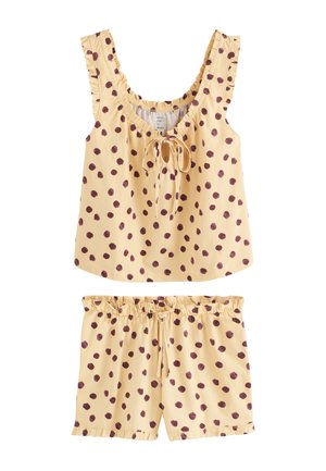 Persoon draagt lichtgeel pyjamaset met donkerpaarse stippen, tilt het bovenstuk op om de buik te laten zien, elastische korte broek met koord in de taille.