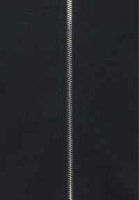 Marinblå zip-up jacka med en silverfärgad metallblixtlås i mitten, texturerad tyg och ribbad design.