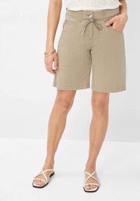 Shorts beiges avec une taille à cordon de serrage, des poches latérales et une coupe décontractée. Associés à des sandales blanches minimalistes avec des lanières croisées.