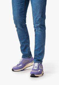 Sneaker viola realizzati in mesh e pelle scamosciata, con lacci bianchi, suola ammortizzata e un accento grigio sul lato. Abbinati a jeans blu.