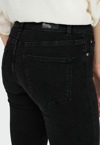 Vaqueros de mezclilla negra con un diseño de altura media, estilo de cinco bolsillos y costuras del mismo tono. Incluye una etiqueta tejida en la cinturilla.