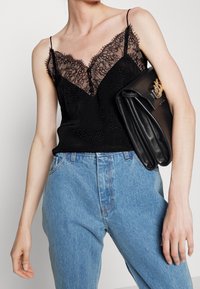 Černý top s krajkovým lemem, tenké ramínka a texturovaný vzor, v kombinaci se světle modrými džíny s vysokým pasem a černým psaníčkem.