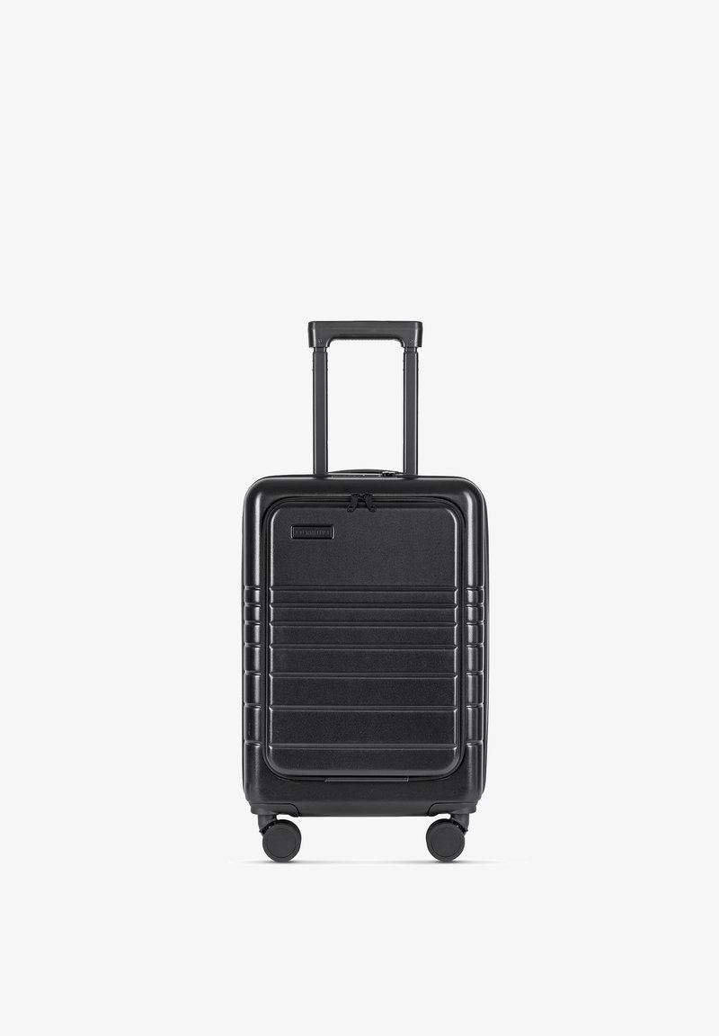 Zwarte harde koffer met een gestructureerd oppervlak, horizontale ribbels, uitschuifbare handgreep en vier wielen voor mobiliteit.