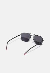 Sunglasses med svart metallram, tonade linser och röda gummitippar på skalmarna. Fyrkantig form med en minimalistisk design.