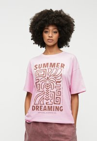 Light pink cotton t-shirt with short sleeves, featuring a brown graphic design with the text "SUMMER DREAMING" and geometric patterns.