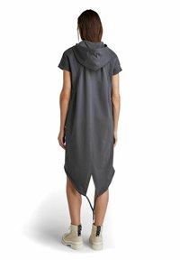 Grå huvtröja med korta ärmar, asymmetrisk fåll och dragsnören, tillverkad av ett mjukt, strukturerat tyg. Bärs med beige stövlar.