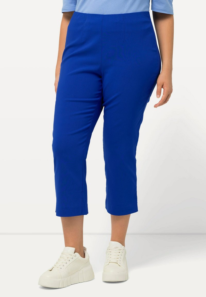 Pantaloni blu a vita corta realizzati in tessuto elasticizzato, con una texture liscia e una cintura aderente. Abbinati a sneaker bianche.