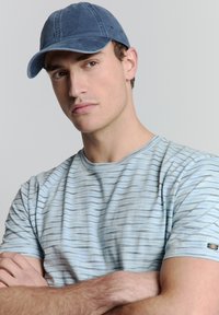 Blauwe katoenen pet gecombineerd met een blauw gestreept shirt met korte mouwen. Het shirt heeft een ronde halslijn en subtiele horizontale patronen.