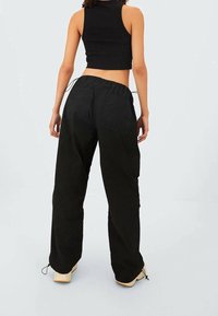 Zwarte high-waisted broek met een losse pasvorm, gemaakt van stevige stof, met een elastische tailleband, twee achterzakken en koordjes aan de onderkant.