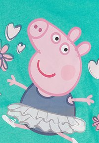 Personaje de Peppa Pig con una camiseta azul y una tutu blanca, sobre un fondo verde azulado con corazones y flores rosadas y azules a su alrededor.