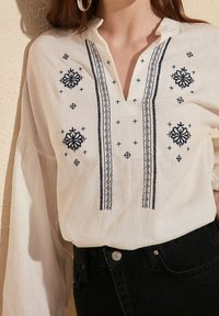 Hvid bluse med sort detaljeret broderi ned foran, lange pufærmer, båret ind i højtaljede sorte jeans.