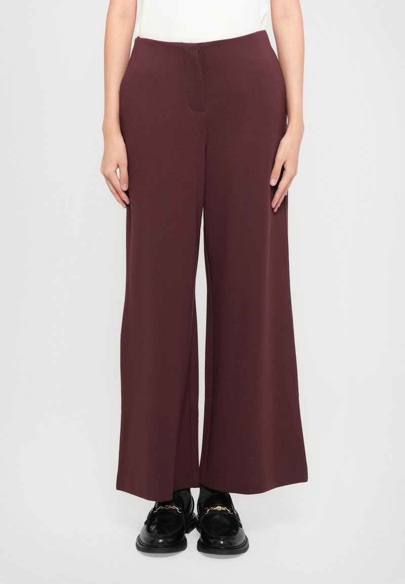Burgundy široke hlače iz gladkega materiala, z ravnim sprednjim delom in stranskimi žepi, v kombinaciji z črnimi loaferji.