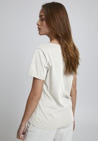 Helle Baumwoll-T-Shirt mit kurzen Ärmeln, runder Halslinie und lockerer Passform, das eine glatte Textur und sauber genähte Kanten aufweist.