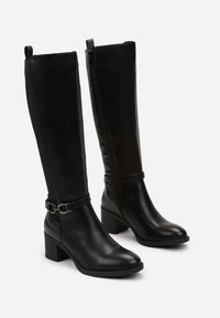 Bottes noires montantes en cuir lisse, dotées d'un talon épais, d'une fermeture éclair latérale et de détails décoratifs de sangle à la cheville.
