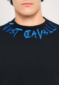 Sweatshirt preto com texto em azul bordado na gola. O tecido é suave, com um colarinho canelado e sem padrões adicionais.