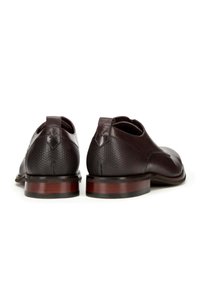Zapatos de piel marrón oscuro con un tacón texturizado y una parte delantera lisa. Tienen un pespunte decorativo y una suela de madera de contraste.