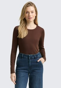Braunes Langarmoberteil mit Rundhalsausschnitt, kombiniert mit hochtaillierten blauen Jeans aus Denim, die einen klassischen Schnitt und sichtbare Nähte aufweisen.