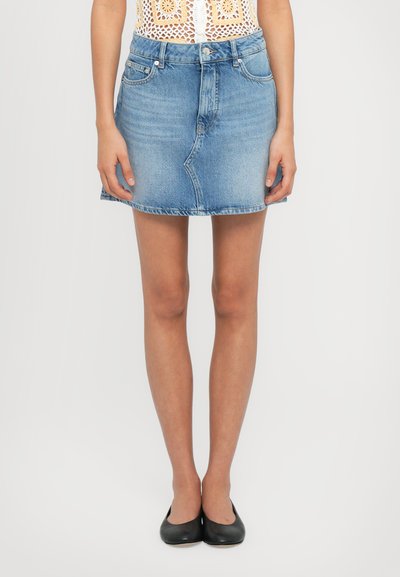 Mini gonna in denim azzurro chiaro con design aderente, orlo strappato e tasche frontali. Abbinata a scarpe nere flat.