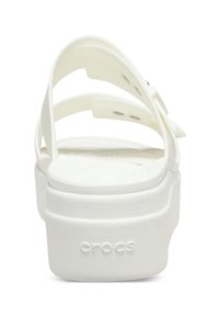 Białe sandały na platformie z dwoma szerokimi, zakrzywionymi paskami. Teksturowana podeszwa z okrągłymi wzorami. Na obcasie wytłoczone logo "Crocs".