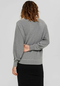 Pull gris tricoté avec manches tombantes, poignets et ourlet côtelés. Texture lisse, coupe décontractée, vue montrant le dos et la position des mains.