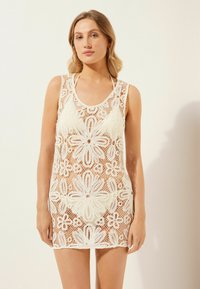 Cubierta de playa blanca de ganchillo con patrones florales, diseño sin mangas y escote redondeado. Textura transparente y ajuste relajado.