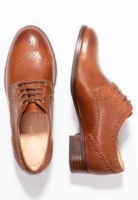 Chaussures oxford en cuir marron avec des bouts arrondis, un design à lacets, des détails de brogue et un talon en bois empilé. Texture lisse.