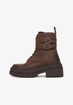 Brązowe skórzane botki za kostkę z okrągłym noskiem, sznurowaniem z przodu oraz podwójnymi paskami z klamrami. Gruba, teksturowana podeszwa z niewielkim obcasem.