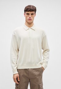 Μπεζ πόλο μπλούζα μακρυμάνικη με γιακά, φτιαγμένη από μαλακό υλικό. Διαθέτει χαλαρή εφαρμογή και απλό σχέδιο, σε συνδυασμό με καφέ cargo παντελόνια.