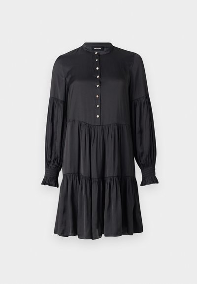 Zwarte jurk met een hoge kraag, knoopsluiting aan de voorkant en lange pofmouwen. Heeft een gelaagde rok en versierde knopen in de vorm van sterren en harten.