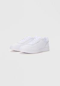 Zapatillas deportivas blancas con parte superior de cuero liso, punta redonda, diseño de cordones de seis ojales, suela de goma de perfil bajo, detalle de marca sutil en el lateral.