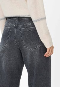 Jeans high-rise grigio scuro con una vestibilità comoda, dotati di due tasche posteriori e una texture scolorita, abbinati a un maglione di colore chiaro in maglia.