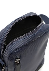 Borsa a tracolla strutturata blu navy con chiusura a zip, cuciture diagonali e tirazip in argento. Interno foderato in materiale nero.