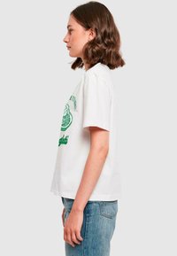 T-shirt en coton blanc avec des manches courtes, un col rond et un imprimé graphique vert sur le devant. Porté avec un jean droit bleu clair.