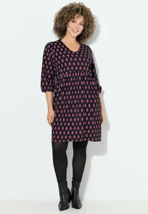 Vestido negro con escote en V, mangas tres cuartos y cintura fruncida. Presenta un patrón geométrico rosa y se combina con medias negras.