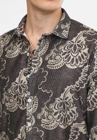 Camicia con bottoni realizzata in un tessuto scuro a motivo, caratterizzata da grandi disegni floreali beige, collo classico e bottoni bianchi per la chiusura.